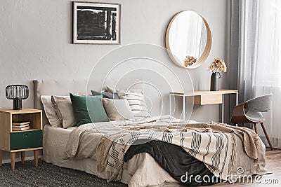 Elegant round mirror in wooden frame above fancy console table with flowers in vase in trendy bedroom interior with beige vase Stock Photo