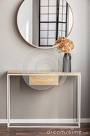 Elegant round mirror in wooden frame above fancy console table with flowers in vase in trendy bedroom interior with beige vase Stock Photo