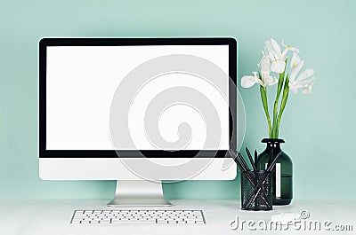 Elegant spring home workplace with blank computer screen, black stationery, keyboard, mouse, white fresh flowers in vase in green. Stock Photo