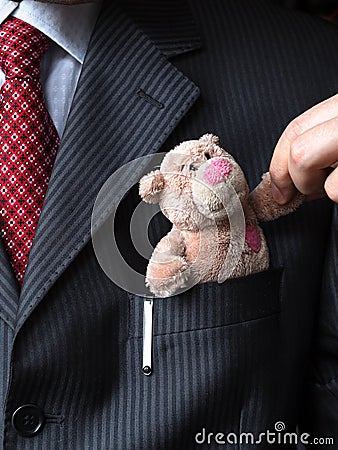 The elegant stylish businessman keeping cute teddy bear in a his breast suit pocket. Hand shaking teddy bear's paw. Formal n Stock Photo