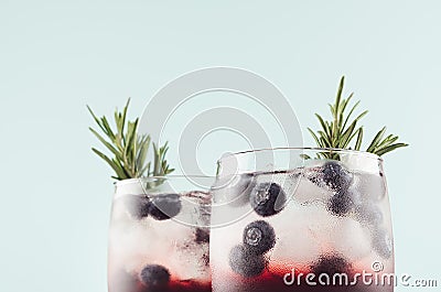 Elegant summer fresh drinks with ice cubes, blueberry, rosemary on fashion pastel mint color background, closeup, top section. Stock Photo