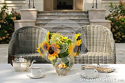 Elegant tea serving in garden with sunflowers in vase on marble table with silver tea pot and cookies Stock Photo
