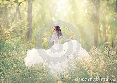 Elegant and tender girl with black hair in white elegant light dress, lady runs in forest, turning pretty face on camera Stock Photo