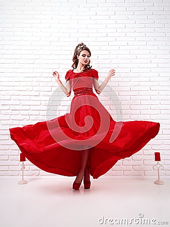 elegant woman in a long flittering red dress is standing in a white room Stock Photo