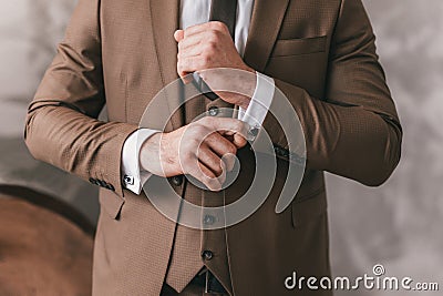 Elegant young fashion man looking at his cufflinks while fixing them. Photo of male hands. Handsome groom dressed in brown formal Stock Photo