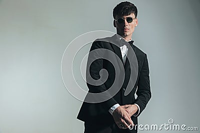 elegant young guy in black tuxedo with glasses adjusting sleeve Stock Photo