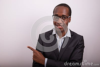Elegantly dressed african businessman wears eyeglasses and points his finger to left. Advertising concept Stock Photo