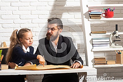 Elementary funny pupil girl with serious teacher in classroom. Fathers and daughters learning. Doing homework with dad. Stock Photo