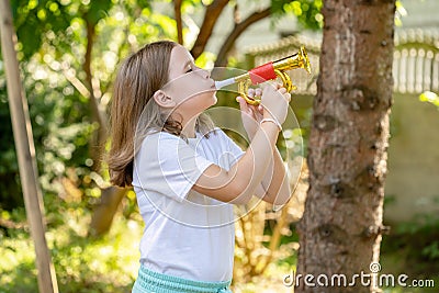 Elementary school age girl playing a toy trumpet prop, holding it in hands doing a bugle call signal. Simple calling, call to arms Stock Photo