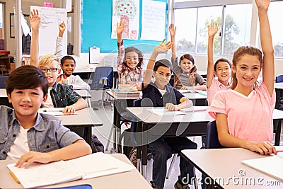 Elementary school kids in a classroom raising their hands Stock Photo