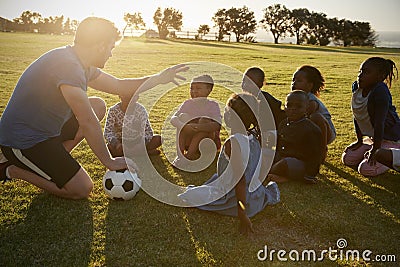 Elementary school kids and teacher sitting with ball in field Stock Photo