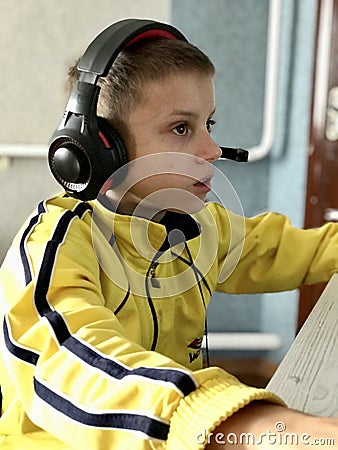 an eleven-year-old boy in headphones sits at the computer in the evening and plays games and studies Stock Photo