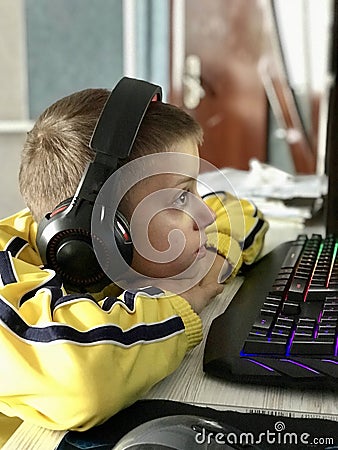 an eleven-year-old boy in headphones sits at the computer in the evening and plays games and studies Stock Photo