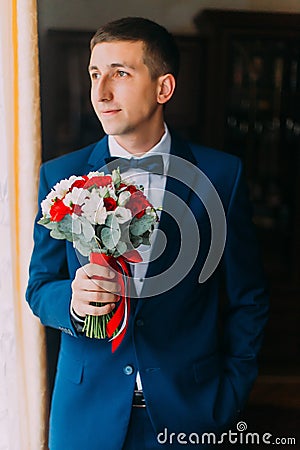 Ellegant bridegroom in blue suit with bow-tie holding a bouquet forward to meeting his bride Stock Photo