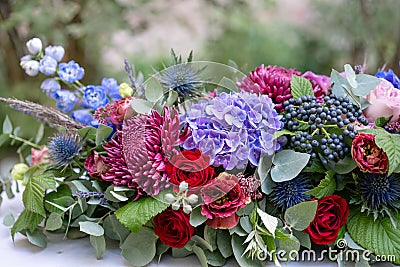Elongated floral arrangement in vintage metal vase. table setting. Blue and red color. Gorgeous bouquet of different Stock Photo