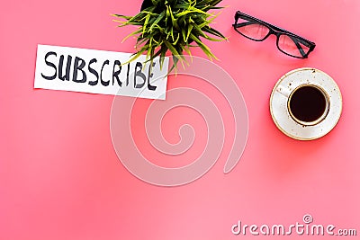 Email subscribe concept. Hand lettering subcribe on work desk with plant, glasses, cup of coffee on pink background top Stock Photo