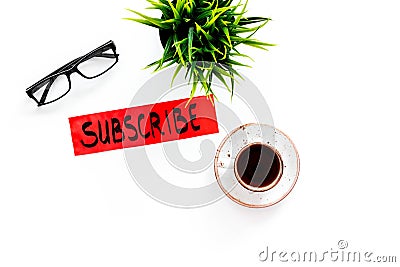 Email subscribe concept. Hand lettering subcribe on work desk with plant, glasses, cup of coffee on white background top Stock Photo