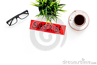 Email subscribe concept. Hand lettering subcribe on work desk with plant, glasses, cup of coffee on white background top Stock Photo