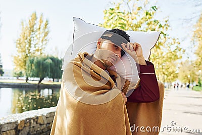 Embracing the pillow. Young man in pajama is outdoors on the street. Feels sleepy Stock Photo