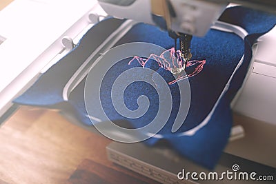 Embroidery hoop of a sewing machine where boiled wool in classic blue color is being equipped with pink magnolia embroidery Stock Photo