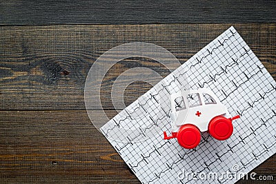 Emergency care concept. Ambulance vehicle toy near cardiogram on dark wooden background top view space for text Editorial Stock Photo