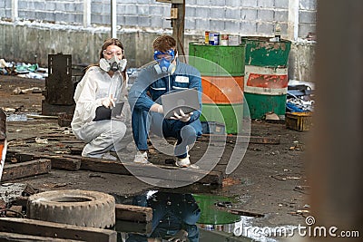 emergency pollution factory concept. engineers wearing mechanic jumpsuits and ppe and gas masks inspect oil on the factory floor Stock Photo