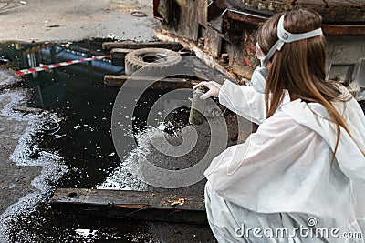 emergency pollution factory concept. Female chemist wearing PPE and gas mask inspecting oil on factory floor Stock Photo
