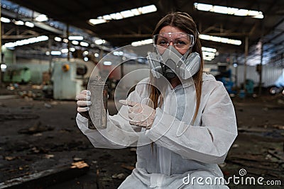 emergency pollution factory concept. Female chemist wearing PPE and gas mask inspecting oil on factory floor Stock Photo