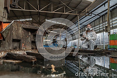 emergency pollution factory concept. Female chemist wearing PPE and gas mask inspecting oil on factory floor Stock Photo