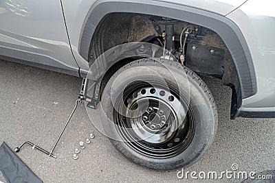 Emergency repairs on the road. Replacing a punctured wheel with a temporary car wheel on the road Editorial Stock Photo