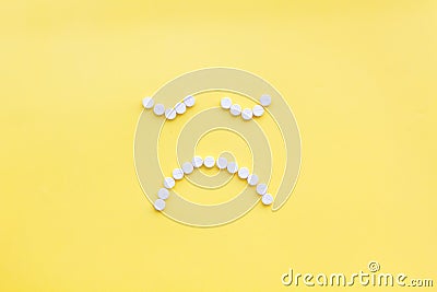 Emotion management concept. Overcome depression. Sad face lined with pills. Yellow background top view copy space Stock Photo