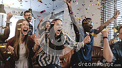 Emotion. Multi-ethnic fans celebrate winning. Confetti 4K slow motion. Passionate supporters shout watching game on TV. Stock Photo