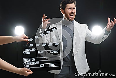 Emotional actor performing while second assistant camera holding clapperboard on black background, closeup Stock Photo