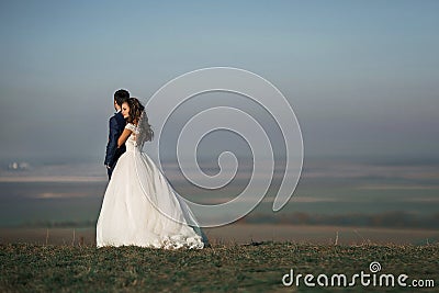 Emotional beautiful bride hugging newlywed groom from behind at Stock Photo