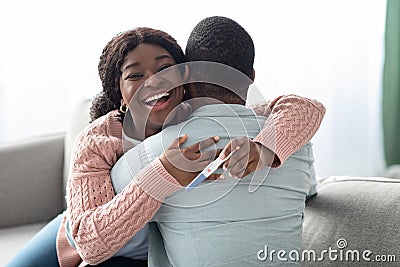 Emotional black woman with pregnancy test hugging her husband Stock Photo