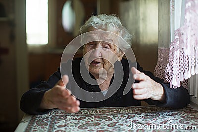 Emotional elderly woman tells gesturing sitting at a table Stock Photo