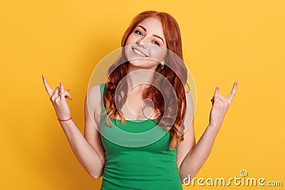 Emotional female makes rock n roll gesture, enjoys cool music at party, demonstrates hand gesture, dressed green outfit, models Stock Photo