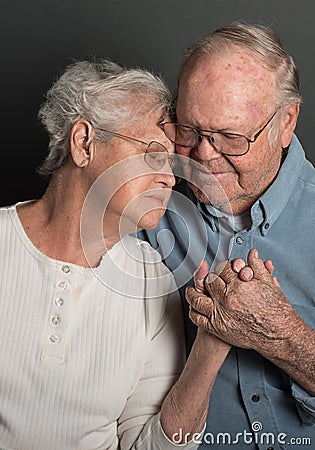 Emotional image of Senior couple holding hands in a tender loving embrace, both wearing glasses, man unshaven Stock Photo