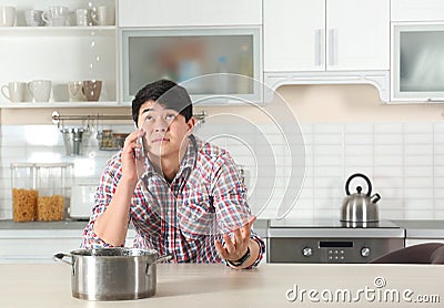 Emotional man calling plumber near table with saucepan under leaking water from ceiling Stock Photo