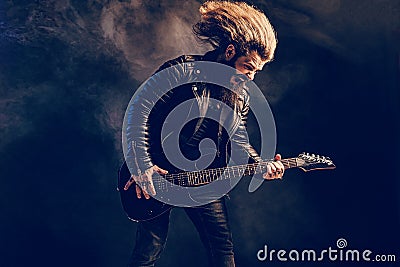 Emotional man rock guitar player with long hair and beard plays on the smoke background. Studio shot Stock Photo