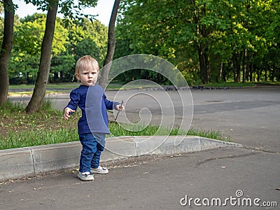 Emotional portrait of an annoyed little blonde girl on a summer day in a city park. Beautiful capricious child Stock Photo