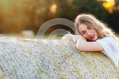 Emotional portrait of a cheerful blonde girl in a countryside landscape with hay rolls in sunset light Stock Photo