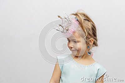 Emotional portrait of a girl in a crown and earrings on a light background. Concept: a little princess, a young fashionista, child Stock Photo