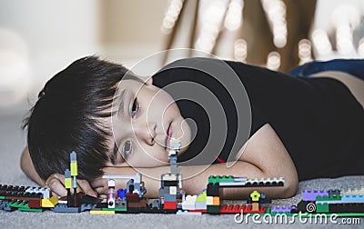 Emotional portrait Unhappy kid lying down on wooden floor with his plastic blocks toy, Candid shot lonely Child boy with sad face Stock Photo