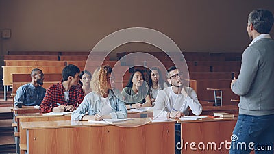 Emotional tutor is speaking to adult students explaining new information while attentive pupils are listening and taking Stock Photo