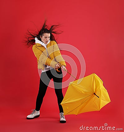 Emotional woman with umbrella caught in gust of wind on red background Stock Photo