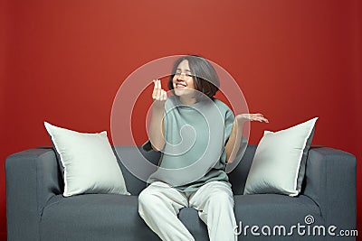 Emotional young beautiful girl show money gesture, asking cash, sitting on sofa. Not enough money. Debt or credit. Stock Photo