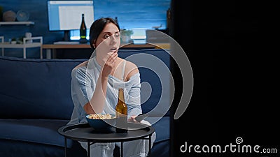 Emotional young woman eating popcorn while watching disgusting tv movie Stock Photo
