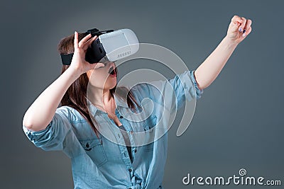 Emotional young woman using a VR headset and experiencing virtual reality on grey background Stock Photo