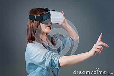 Emotional young woman using a VR headset and experiencing virtual reality on grey background Stock Photo